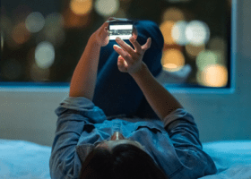 A woman lying down using a dating app on her phone.