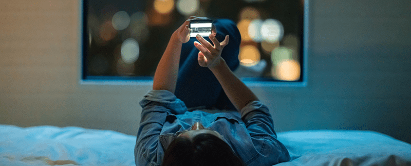 A woman lying down using a dating app on her phone.