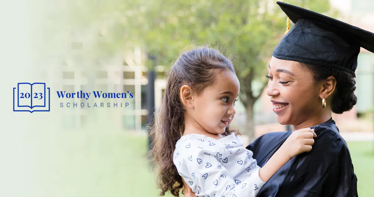 A woman in a graduation cap and gown holding her daughter. Caption reads 2023 Worthy Women's Scholarship.