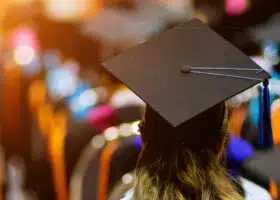 Recent graduate attends a graduation ceremony with their back turned proudly displaying their graduation cap.